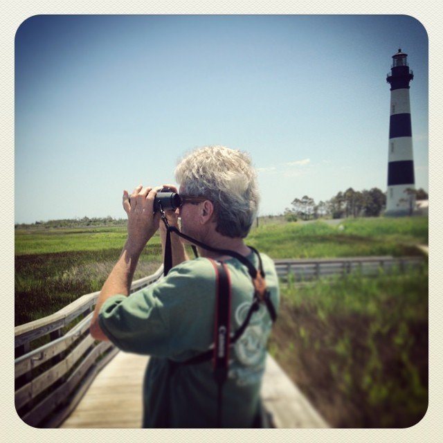 A visitor using binoculars from a flat wooden birding boardwalk at Cape Hatteras National Seashore