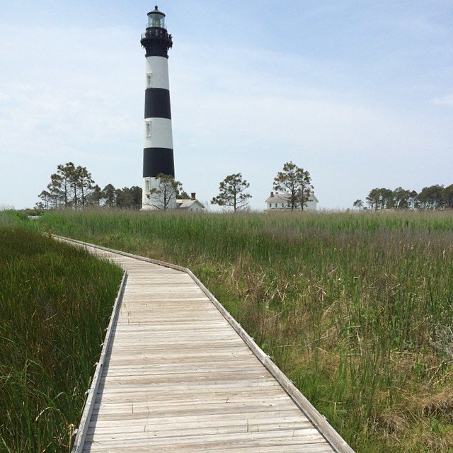 Wooden boardwalk trail leading through marsh grass toward the Bodie Island Lighthouse