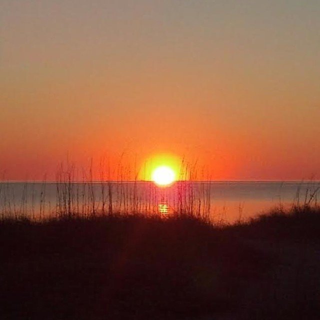 Orange sun setting over the calm water of Pamlico Sound behind marsh grass