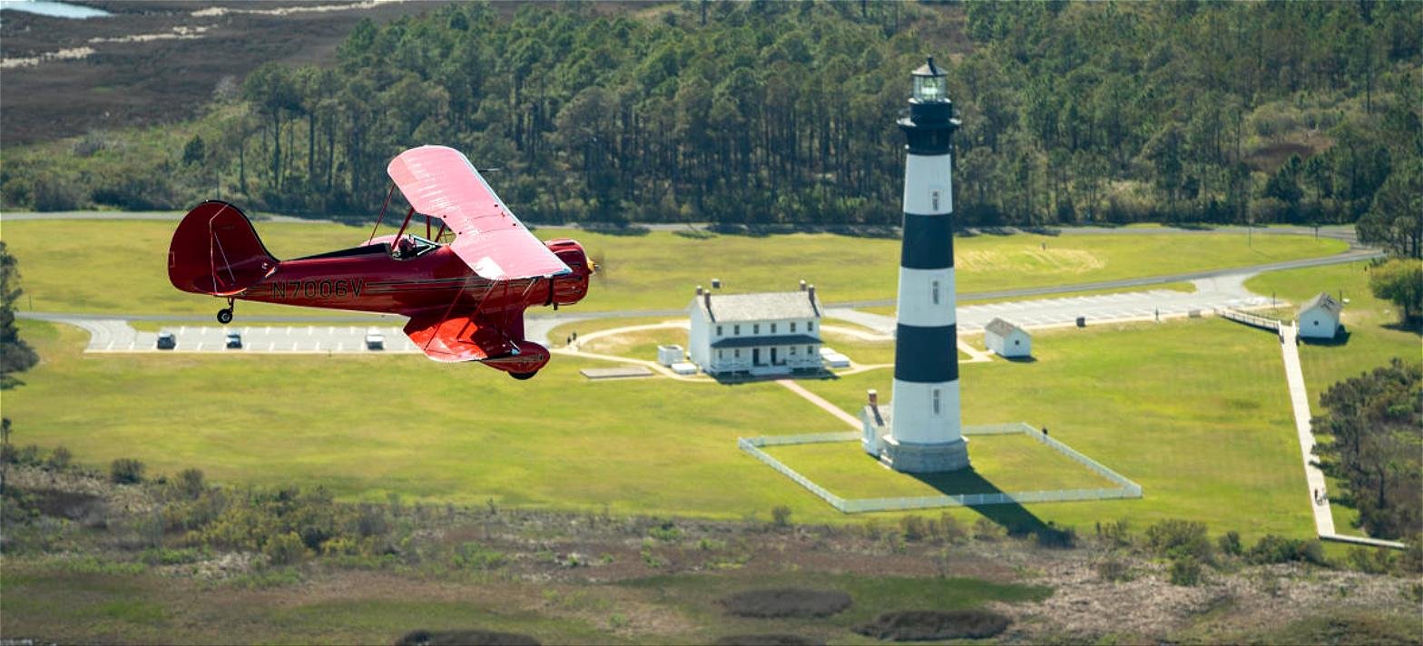 A red WACO biplane flying past Bodie Island Lighthouse on the Outer Banks